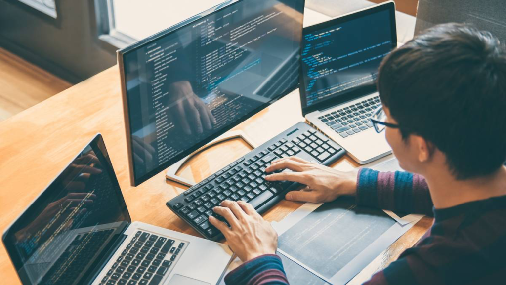 A man writes code on three computers